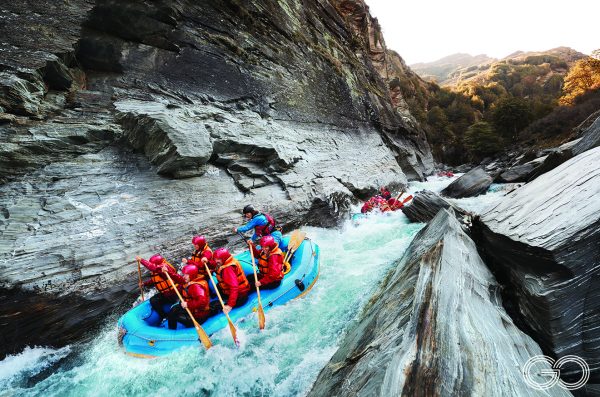 Rafting the Shotover River - a group of people in a blue raft padding on bright blue water